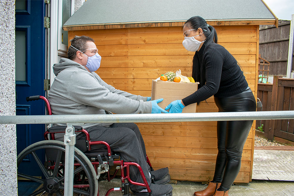 Photo of a woman delivering a box of food to a man at home.